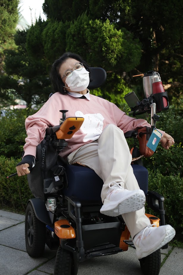 휠체어를 탄 노들장애인야학 학생이 분홍 라운드 티를 입고 포즈를 취한 사진