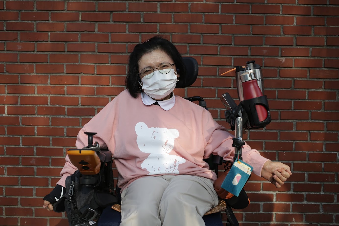 휠체어를 탄 노들장애인야학 학생이 분홍 라운드 티를 입고 포즈를 취한 사진