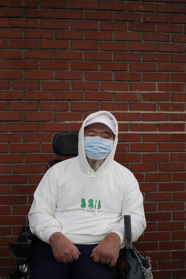 녹색 눈사람(흰색 후드) 을 입고 휠체어에 앉아 양손을 모은 포즈를 취한 노들장애인야학 교장선생님