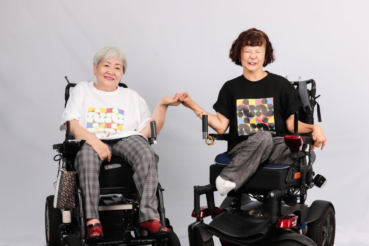 장애인지역공동체 티셔츠를 입고 손을 잡은 두명의 보내는 활동가