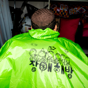 장애 해방 글씨가 대문짝 만하게 등판에 새겨진 판초 우비 초록색 뒷모습 클로즈업.